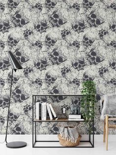 a black and white wallpaper with skulls on it, next to a chair in front of a book shelf