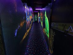 a long hallway with colorful lights and graffiti on the walls, leading to another room