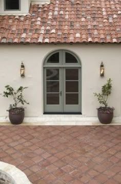 two potted plants on the side of a building with an arched window and tiled roof