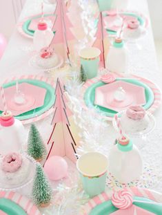 the table is set with pink and green plates, cups, and desserts on it