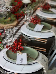 a table set with place cards, silverware and greenery for christmas dinner party