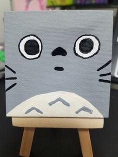 a painting of a cat with big eyes on it's face, sitting on a wooden easel