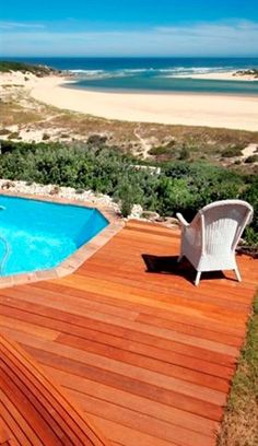 a wooden deck next to a swimming pool with two white chairs on top of it