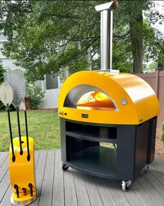 an outdoor pizza oven sitting on top of a wooden deck next to a grill and spatula