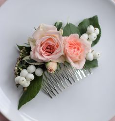 a white plate topped with pink roses and greenery next to a hair comb on top of a table