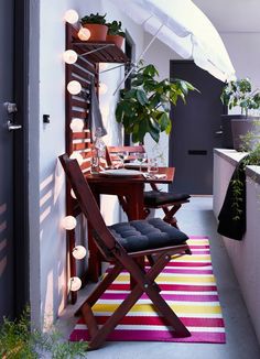 an outdoor dining area with potted plants on the table and striped rug in front