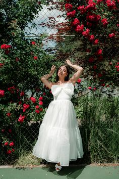 a woman in a white dress standing on a tennis court with her hands behind her head