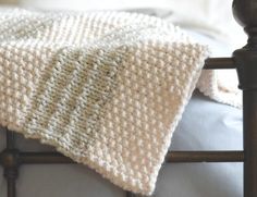 a white knitted blanket sitting on top of a bed next to a wooden headboard