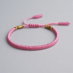 a pink string bracelet with gold beads on a gray background, the cord has been braided together