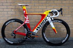 a red and yellow bike parked next to a brick wall