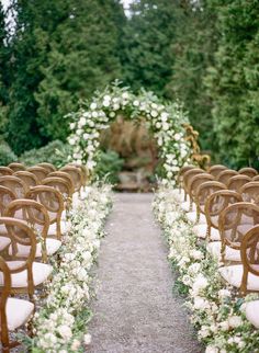 rows of chairs with white flowers and greenery lining the aisle at an outdoor wedding ceremony