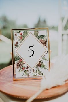 the table numbers are placed on top of a wooden board with white feathers and greenery