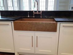 a kitchen sink with black counter tops and white cupboards in front of the window