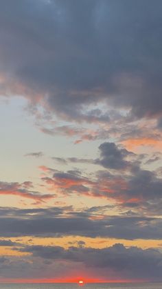 the sun is setting over the ocean with clouds