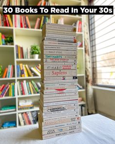 a stack of books sitting on top of a bed in front of a book shelf