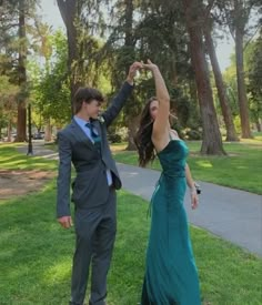 a young man and woman dressed in formal wear standing on grass with their arms raised