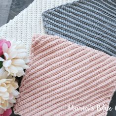 three different colors of knitted blankets with flowers on the top one is pink, grey and white