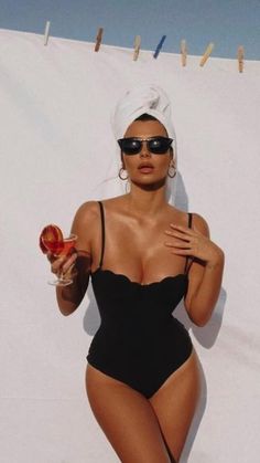 a woman in a black swimsuit holding a glass of wine and standing next to a white wall