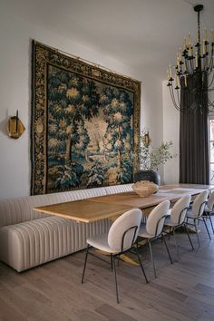 a dining room table with chairs and a tapestry hanging on the wall behind it in front of a chandelier