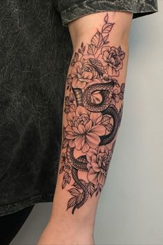 a woman with a snake and flowers tattoo on her arm, holding onto the arm