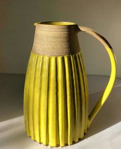 a yellow ceramic pitcher sitting on top of a white countertop next to a wall