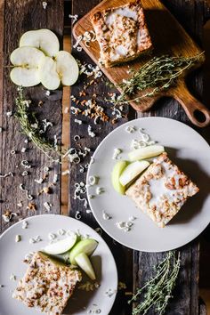 two white plates topped with slices of apple cake next to sliced apples and sprigs of rosemary