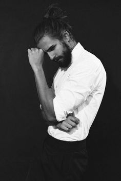 a man with a beard and white shirt is holding his hands to his face while standing against a black background