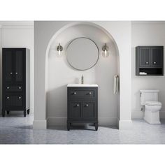 a white toilet sitting next to a sink under a round mirror in a bathroom with black cabinets