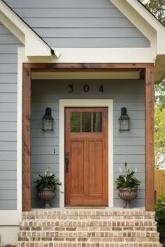 the front door of a blue house with two planters on it's steps