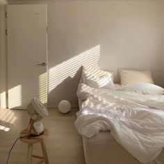 a bed with white sheets and pillows in a bedroom next to a window, fan and door