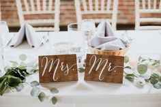 two wooden signs sitting on top of a table next to flowers and greenery in vases