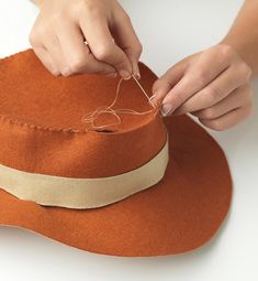 a woman is working on an orange hat with thread and yarn in it's center