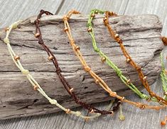 four different colored bracelets sitting on top of a piece of driftwood next to each other