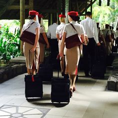 three people in uniforms carrying luggage down a walkway with other people walking behind them on either side