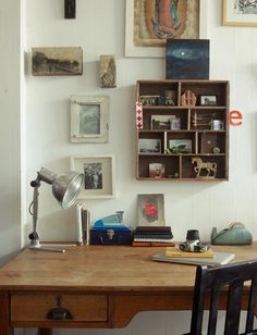 a wooden desk topped with a lamp next to a wall filled with pictures and books