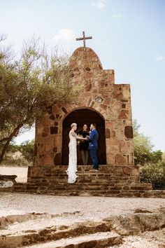 a man and woman standing in front of a stone church with a cross on it