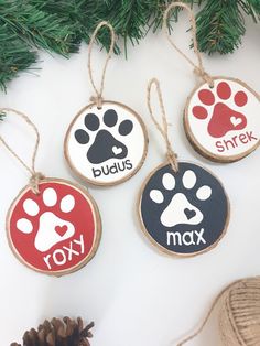 three wooden ornaments with dog paw prints on them, hanging from a christmas tree branch