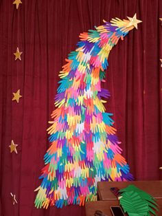 a brightly colored christmas tree made out of handprints on a red curtain background