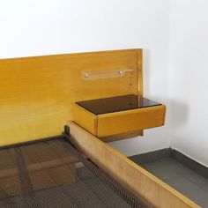 a bed with a wooden headboard and drawers on the bottom shelf, next to a white wall