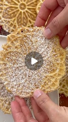 two hands holding a pastry with powdered sugar on top and another hand reaching for it