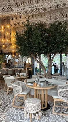 the interior of a restaurant with white wicker chairs and round tables surrounded by trees