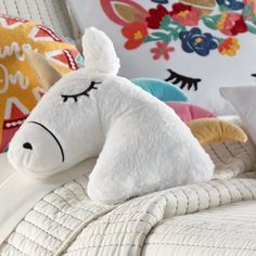 a white stuffed animal laying on top of a bed next to pillows and blankets with colorful designs