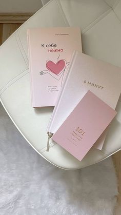 two pink notebooks sitting on top of a white chair next to eachother