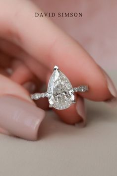 a woman's hand holding an engagement ring with a pear shaped diamond