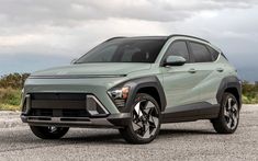 the front end of a light green suv parked on top of a gravel road with mountains in the background