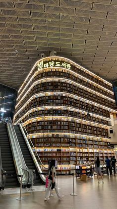 people are walking around in front of an escalator and bookshelf at the airport