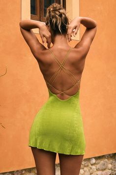 the back of a woman in a short green dress standing next to an orange building