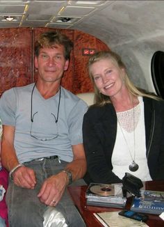 a man and woman sitting on a couch in an airplane with their luggage behind them