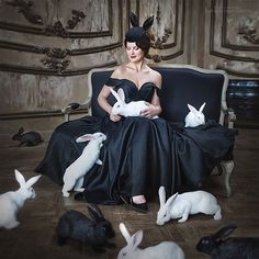 a woman sitting in a chair surrounded by white bunny's and other rabbits, all wearing black