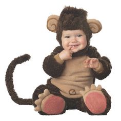 a baby wearing a monkey costume sitting on the ground with his hands in his mouth